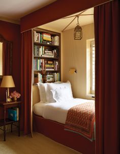 a bedroom with red curtains and a bed in the corner next to a bookshelf