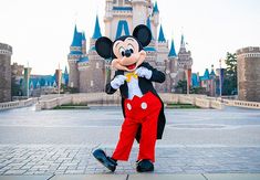 a person in mickey mouse costume standing on the sidewalk near a castle with its front door open