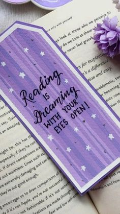 an open book with some flowers on top of it next to a purple and white bookmark