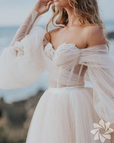 a woman in a wedding dress standing on the beach with her hands behind her head