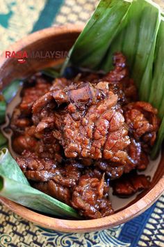 a wooden bowl filled with meat and green onions on top of a table next to leaves