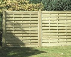 a large wooden fence in the middle of a grassy area with trees and bushes behind it