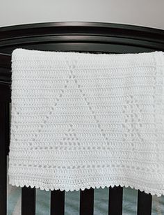 a white crocheted blanket hanging from the side of a crib