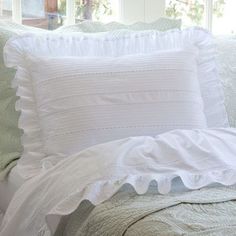 a bed with white ruffled pillows on top of it and a window behind it