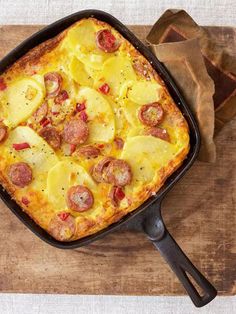 a square casserole with sausage and potatoes in a black pan on a wooden cutting board