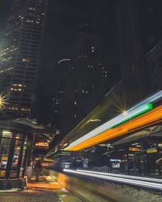 a city street at night with buildings in the background and lights streaking across the road