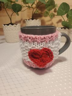 a knitted coffee cup with a heart on the front and sides, sitting on a table