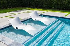 two white lounge chairs sitting in the middle of a pool