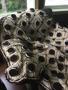 there is a crocheted blanket that has chocolate buttons on it and sits next to a window