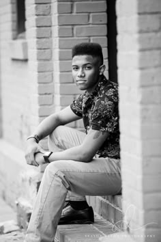 a black and white photo of a young man sitting on the steps in front of a brick building