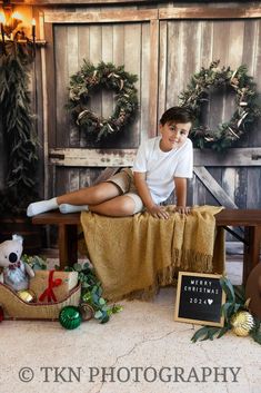 a young boy sitting on a bench in front of christmas wreaths and other decorations