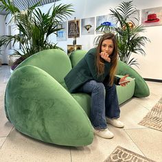 a woman sitting on top of a green couch in a room filled with potted plants