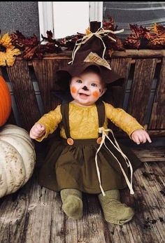 a baby dressed as a scarecrow sitting on a porch with pumpkins and gourds