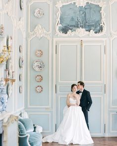 a bride and groom posing for a photo in front of a blue painted room with ornately decorated walls