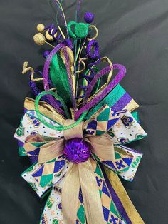 a purple, green and gold bow with flowers on it's side sitting on a black surface