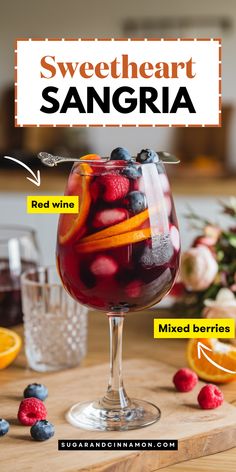 a glass filled with red wine and mixed berries on top of a wooden cutting board