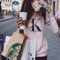 a woman eating a hot dog and drinking starbucks coffee while walking down the street with her hand in her mouth