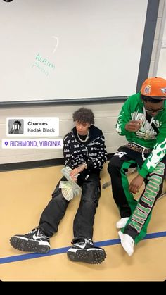 two young men sitting on the floor in front of a white board with writing on it