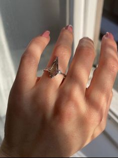 a woman's hand with a diamond ring on her left hand, in front of a window