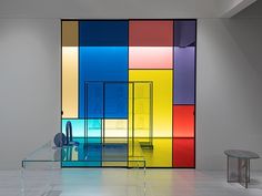 a glass table in front of a multicolored wall with a bench and side table