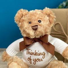 a brown teddy bear wearing a white sweater with the words thinking of you on it