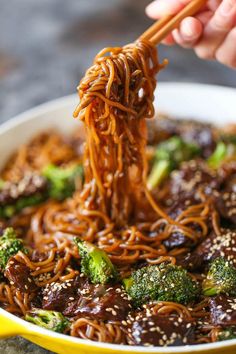 the noodles and broccoli are being held up by chopsticks in order to eat