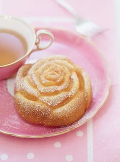 a pink plate topped with a pastry next to a cup of tea