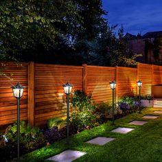 an outdoor garden at night with lights on the fence and grass in the foreground