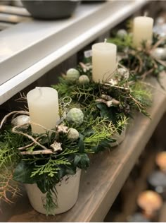 some white candles are sitting on a shelf with greenery and other decorations around it