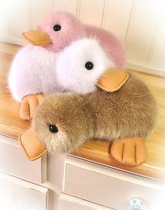 three stuffed animals sitting on top of a wooden shelf next to each other in front of a white wall