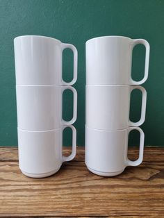 two white coffee mugs sitting on top of a wooden table next to a green wall