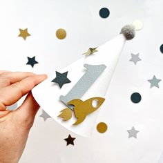 a hand holding a paper party hat with gold and silver stars on the side that says 1