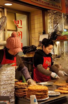 two people preparing food in a kitchen with lots of tin foil on the counter top