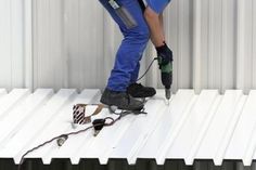 a man in blue overalls and safety gear working on the roof of a building