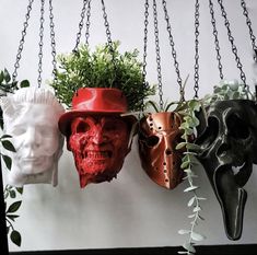 three masks are hanging from chains with plants in them and one is wearing a red hat