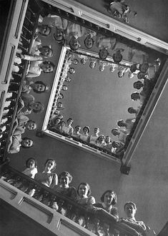 black and white photograph of people looking up at the ceiling in a room filled with dolls