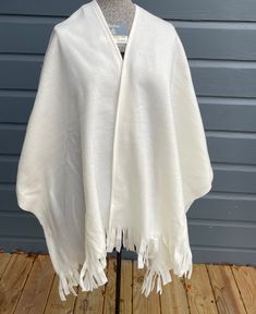 "New without tag crème white poncho scarf with an open front. It will layer flawlessly over any outfit. Just put around your shoulders for a complete cover. Offers exceptional warmth and comfort. Great for a number of stylings and perfect to stay warm in the winter! Measurements in inches: Front length 32\". Back length 32\". Total width 48\". Front panel width 22.5\". The fringe is 4-1/2\"L. 100% polyester. Made in Germany. In excellent unused condition. The photos are an integral part of the d White Cozy Winter Poncho, Oversized Fringed Shawl For Winter, Oversized Fringe Shawl For Winter, Winter Cape With Scarf In Shawl Shape, Winter Fringe Cape Shawl, White Oversized Winter Poncho, Oversized White Poncho For Winter, White Fringed Winter Shawl, White Winter Poncho Cape