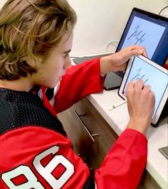 a young boy sitting at a desk using an electronic device with writing on the screen