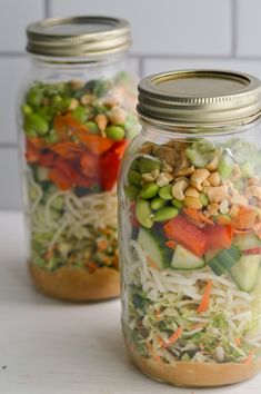 two mason jars filled with salads and veggies sitting on a counter top