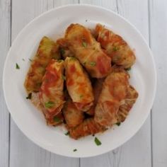 a white plate topped with dumplings covered in sauce and garnished with parsley