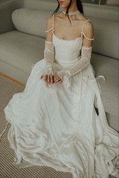 a woman sitting on the floor in a white dress with long sleeves and an open shoulder