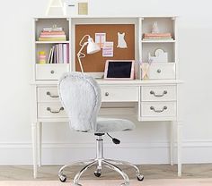 a white desk chair sitting in front of a computer desk with a cork board on it