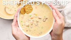 two hands holding a bowl of shepherd's pie soup with crackers in it