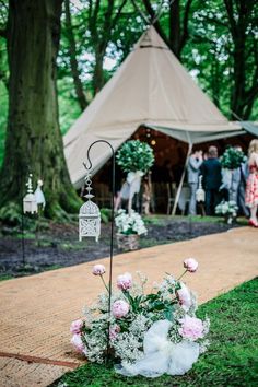 a wedding ceremony in the woods with flowers on the ground and a teepee tent