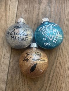 three ornaments with writing on them sitting on a wooden table next to another ornament