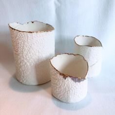 three white vases sitting next to each other on top of a pink table cloth