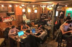 a group of people working on laptops in a room with wooden floors and walls