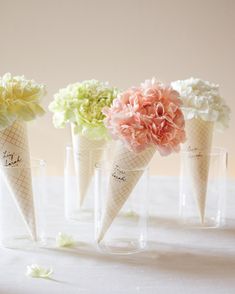 four ice cream cones filled with flowers on top of a white tableclothed surface