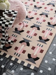 a pink rug with black and white geometric designs on the floor next to a table