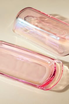 two pink glass containers sitting next to each other on a white counter top and one is empty